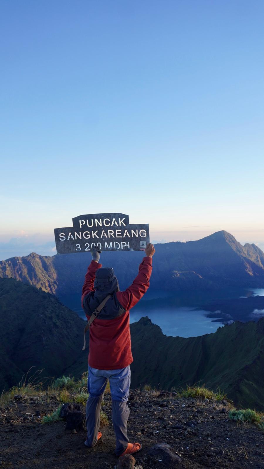 Trekker holding the Puncak Sangkareang summit sign at 3,200m